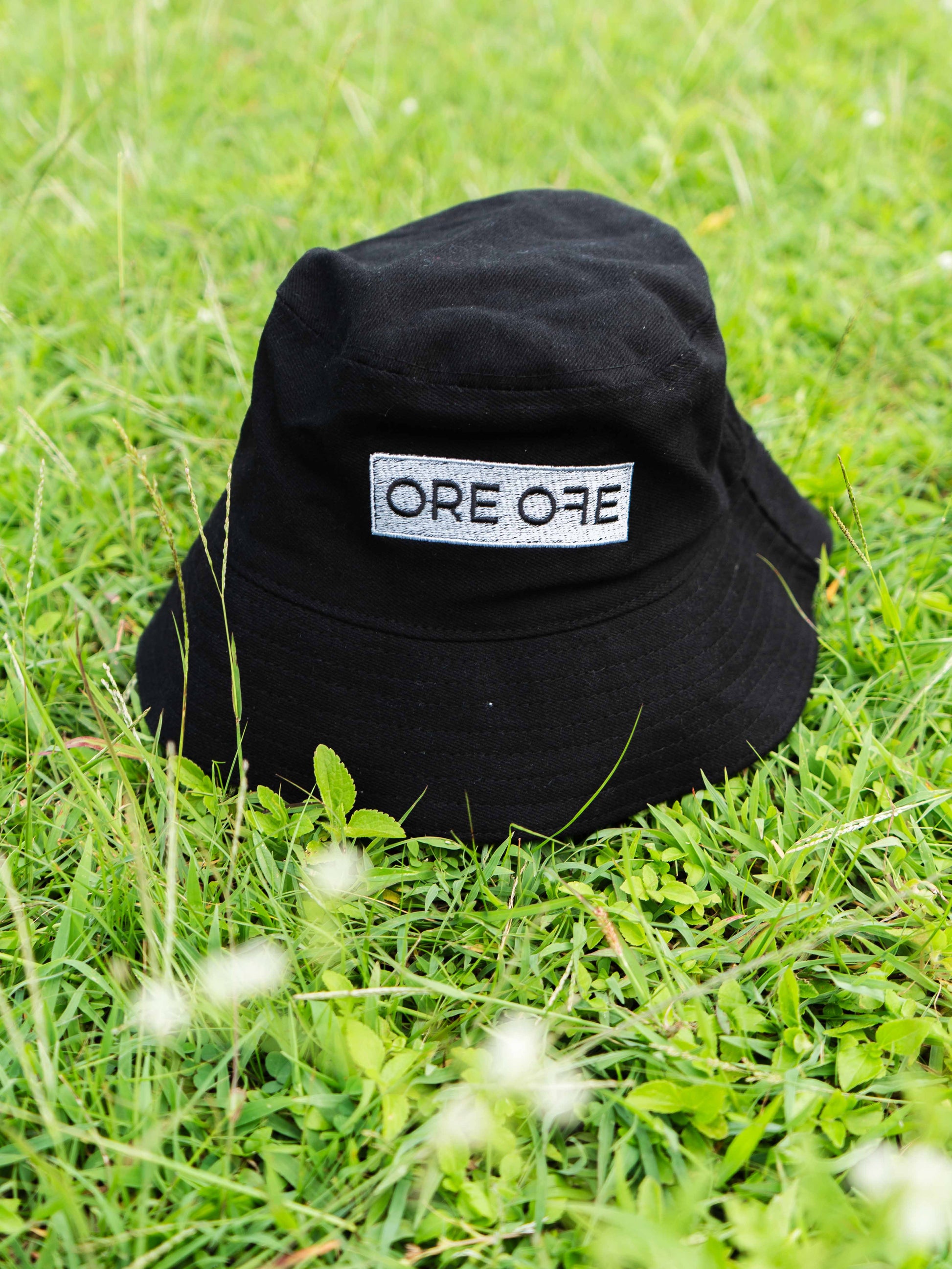 Black bucket hat with 'ORE ORE' logo on grass