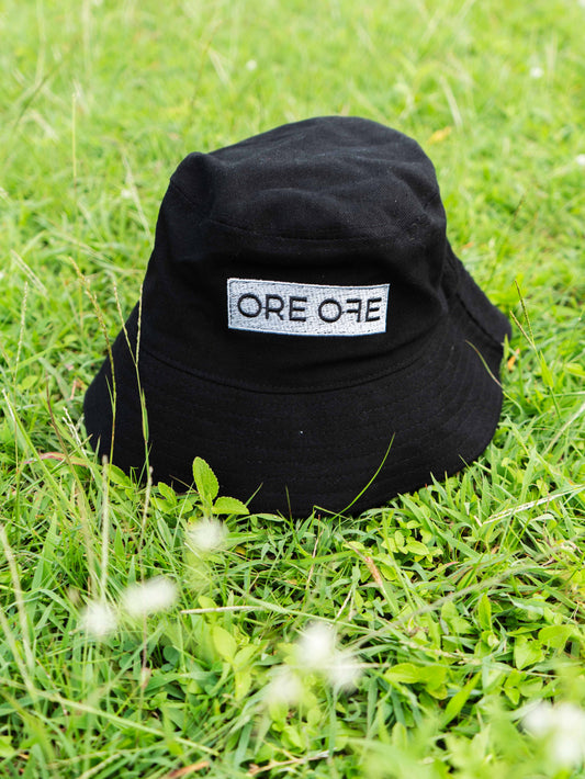 Black bucket hat with 'ORE ORE' logo on grass
