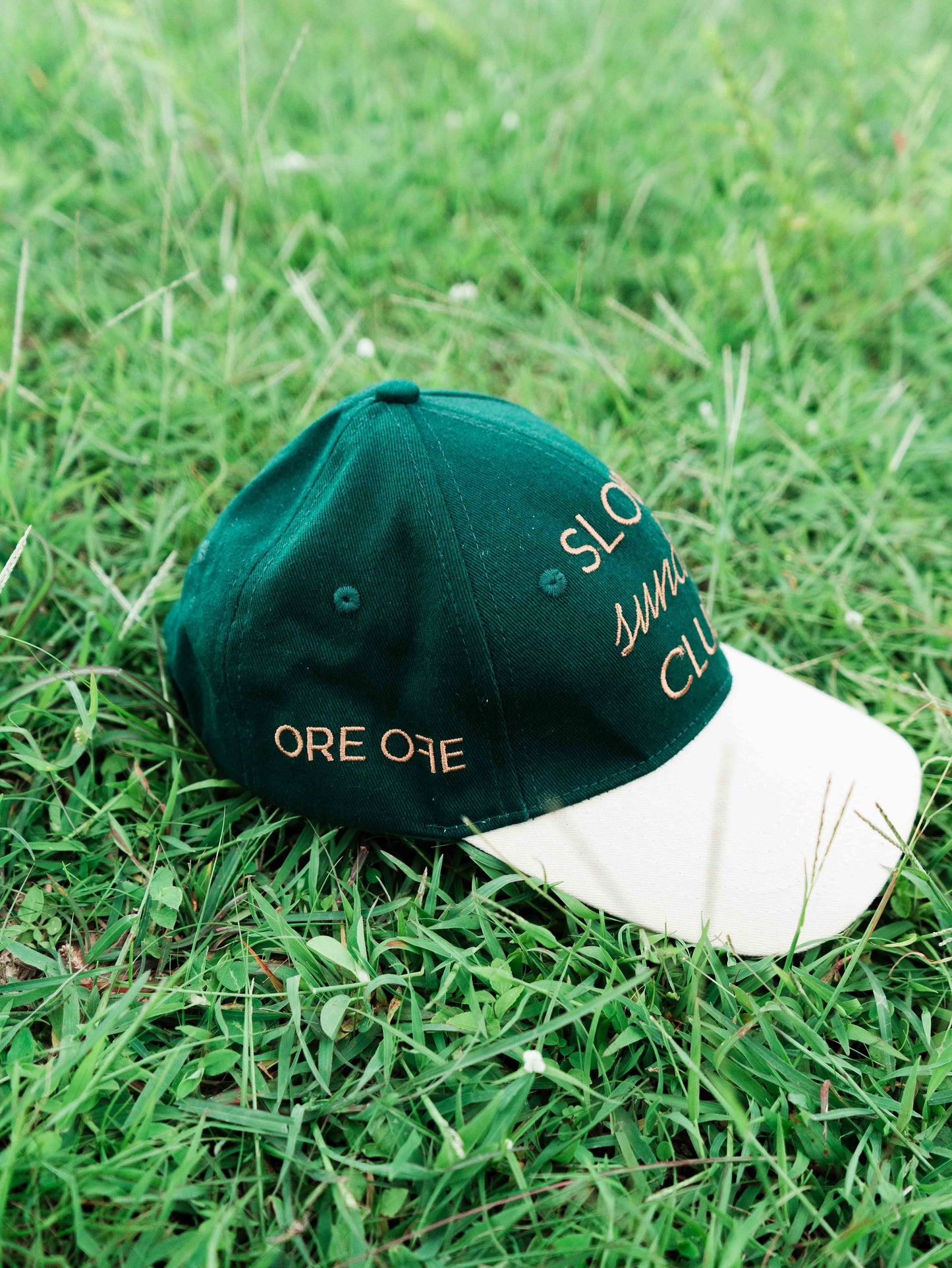 Green and white ORE OFEbaseball cap with 'Slow Sunday Club' text on grass