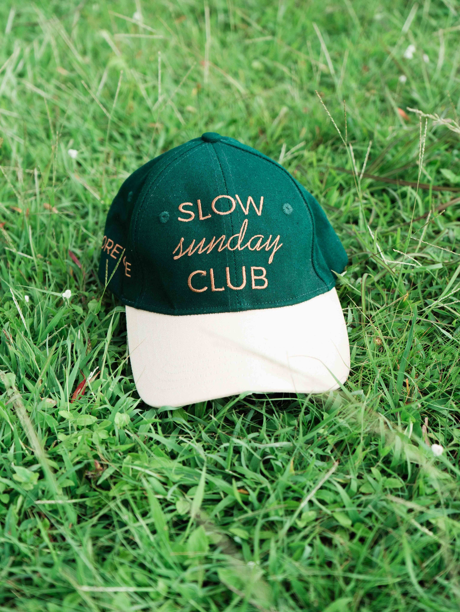 Green and white ORE OFEbaseball cap with 'Slow Sunday Club' text on grass
