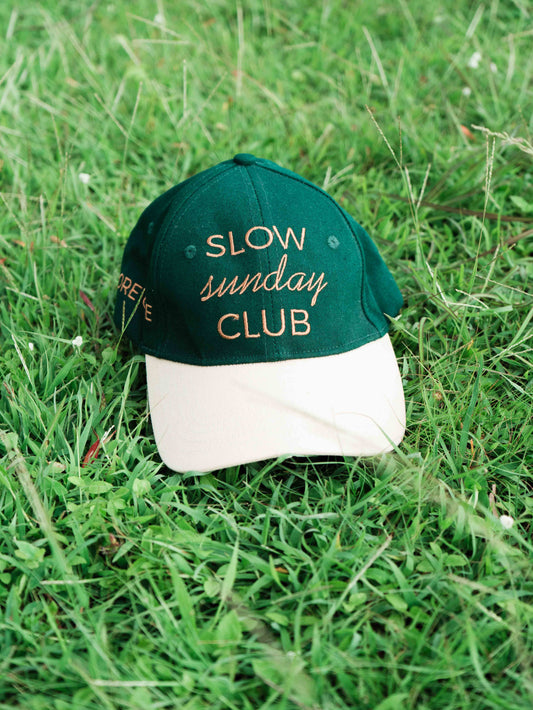 Green and white ORE OFEbaseball cap with 'Slow Sunday Club' text on grass