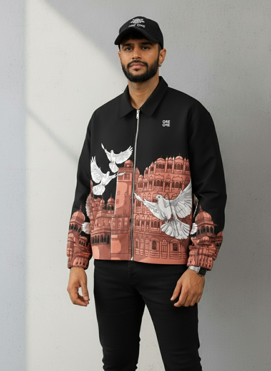 Man wearing a black jacket with a graphic design of a building and birds, standing against a plain background.