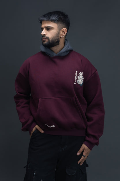 Person wearing a maroon contrast hoodie by ORE OFE with chest & back puff printed design  standaing against  a dark grey background