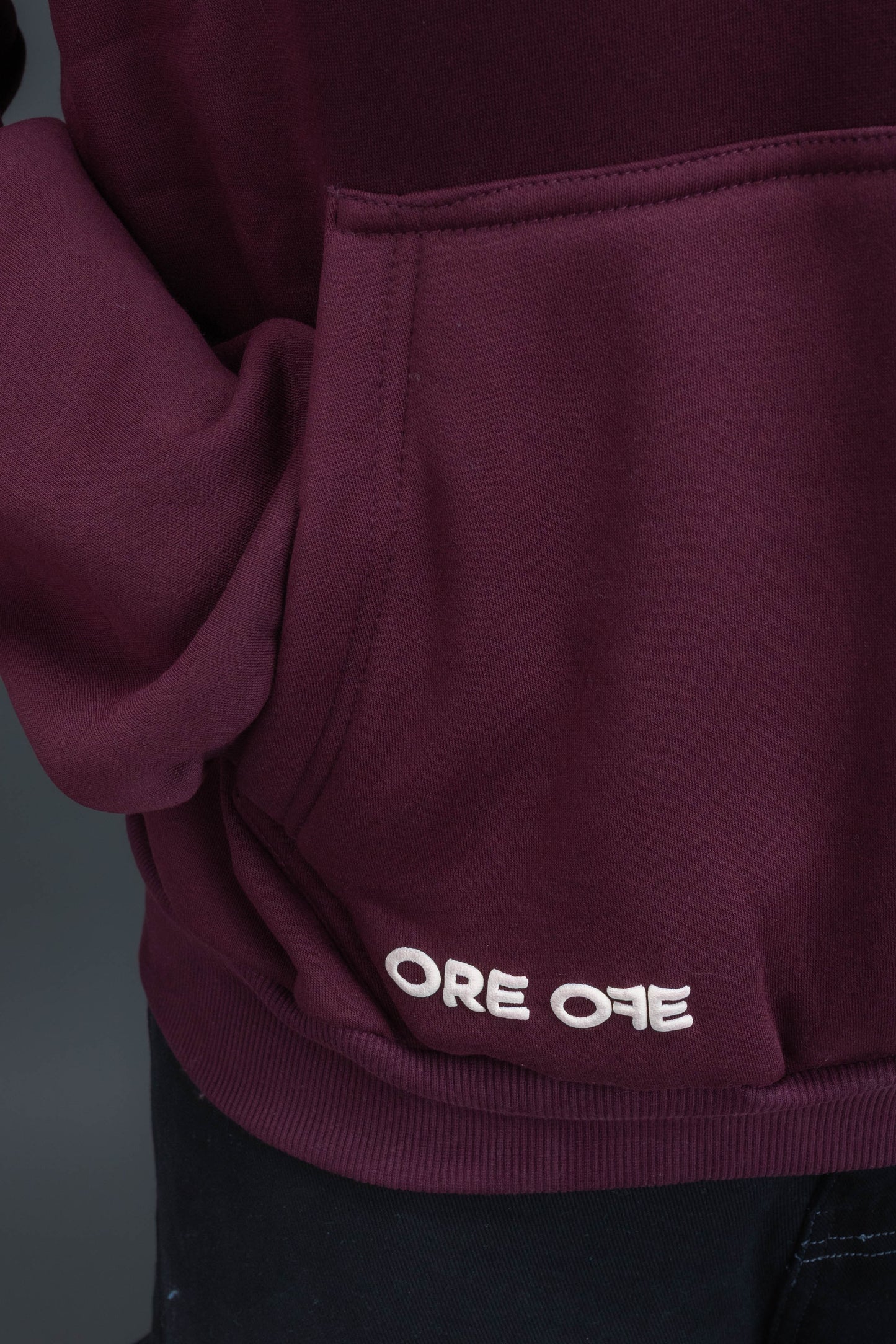 Person wearing a maroon contrast hoodie by ORE OFE with chest & back puff printed design  standaing against  a dark grey background