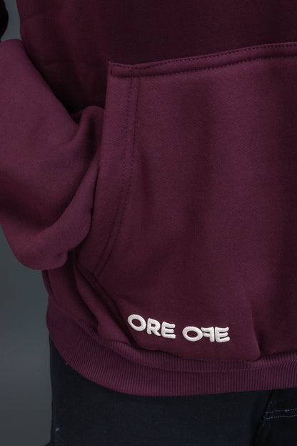 Person wearing a maroon contrast hoodie by ORE OFE with chest & back puff printed design  standaing against  a dark grey background