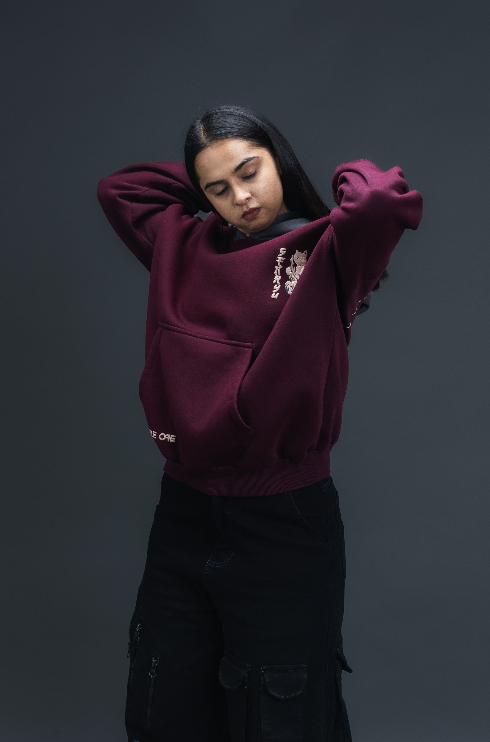Person wearing a maroon contrast hoodie by ORE OFE with chest & back puff printed design  standaing against  a dark grey background
