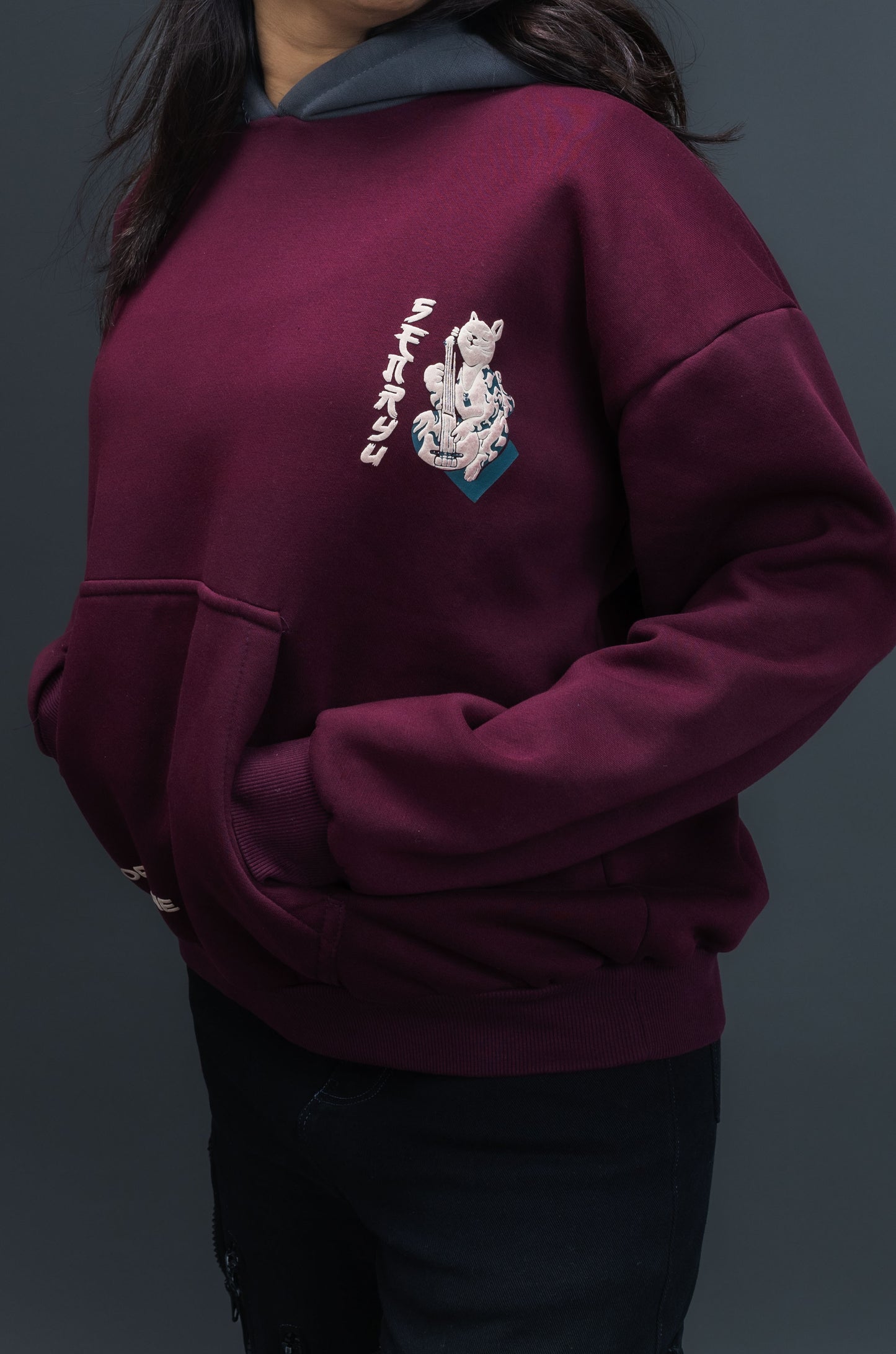 Person wearing a maroon contrast hoodie by ORE OFE with chest & back puff printed design  standaing against  a dark grey background